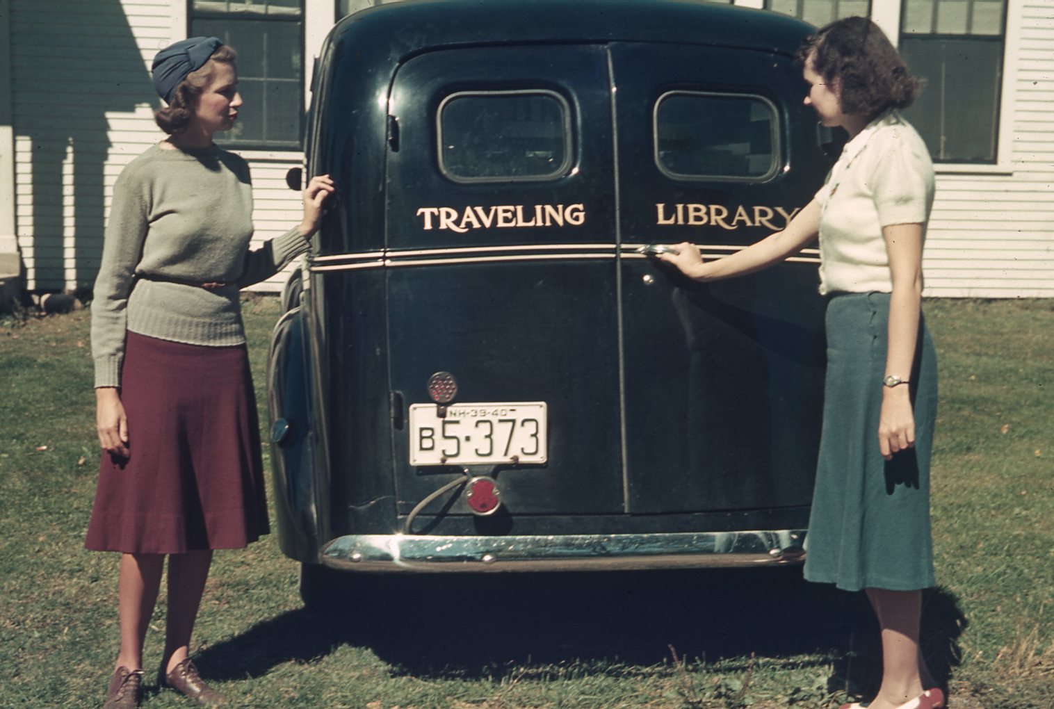 Two women stand at the rear doors of the bookmobile.